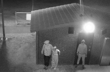 black and white surveillance photo of three individuals with their backs to a public washroom building