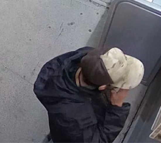 Suspect man wearing a black hooded jacket, a brown and beige camouflage cap and a black necklace.