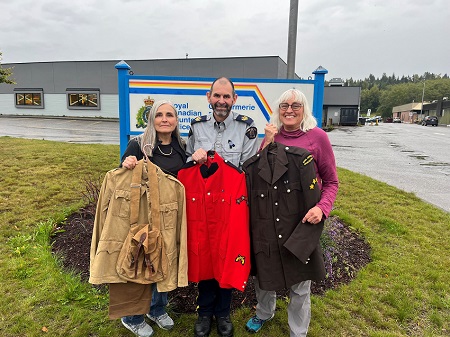 Daughters of teh late James Smythe and Sgt Gardner in front of the Kitimat RCMP detachment holding different era RCMP tunics
