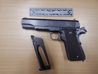 Photo of a black metal pellet pistol with a brown handle and the magazine ejected, below a grey ruler for perspective